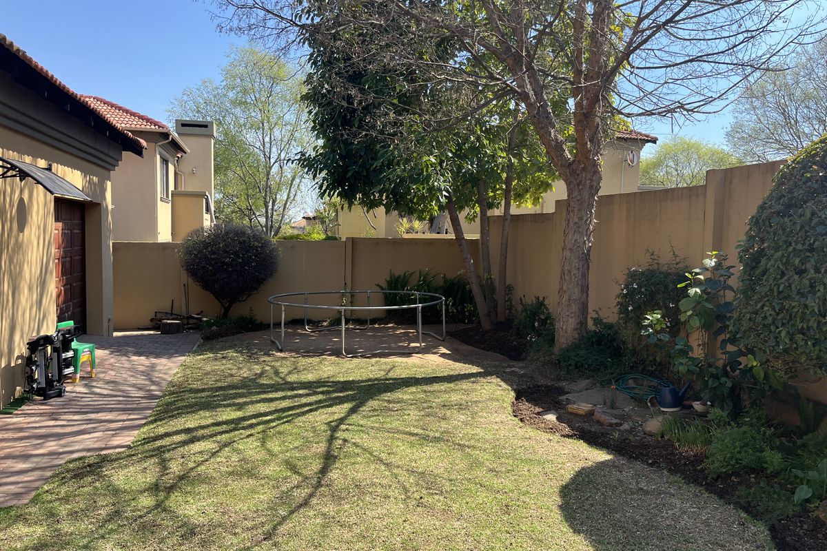 A private rear garden featuring a paved patio area, established trees, and a lawn enclosed by high perimeter walls.