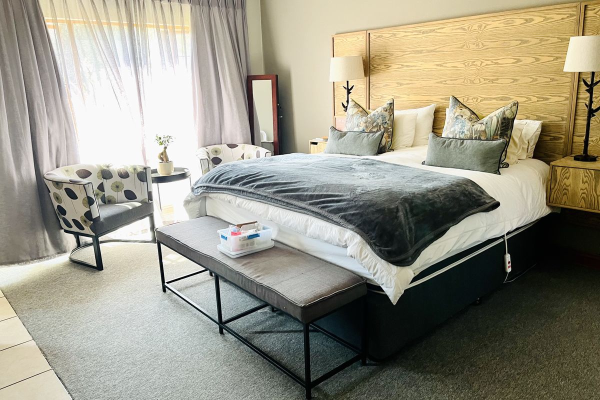 Spacious bedroom featuring a large built-in wooden headboard, wall-mounted lighting, and neutral carpeting with direct access to natural light through large windows.
