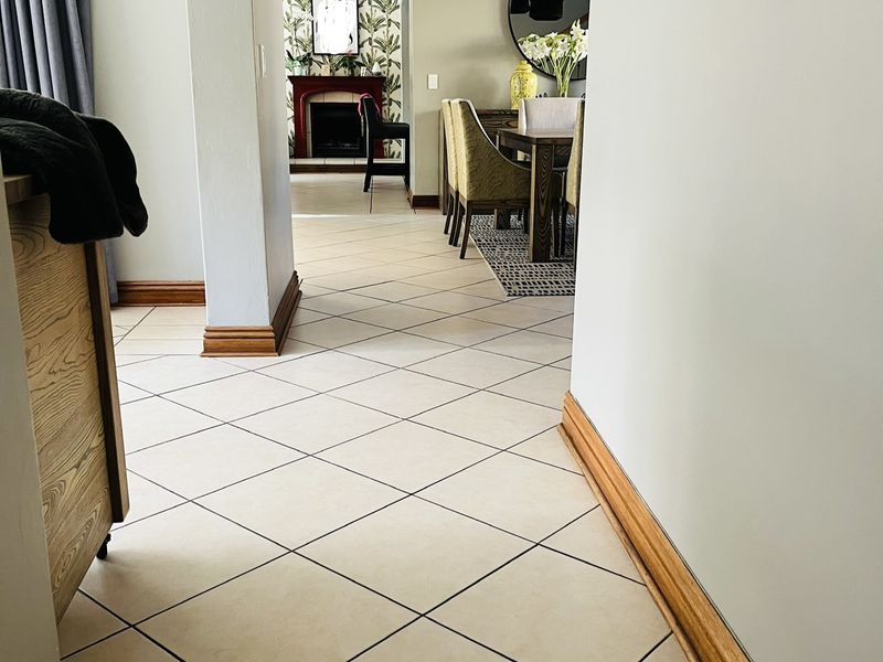 A bright hallway featuring diamond-patterned floor tiles and timber skirting boards, leading through to an open-plan dining area with a fireplace.