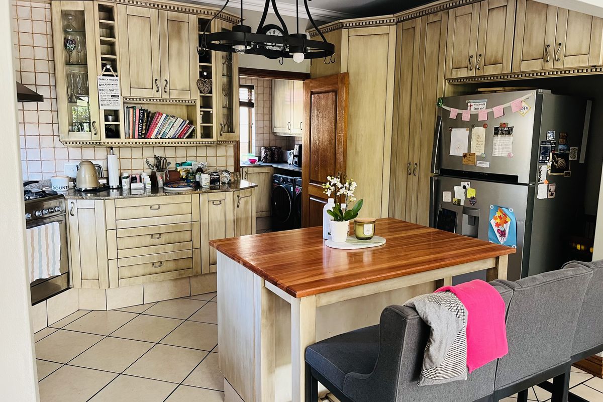 A traditional kitchen featuring light wood cabinetry, granite countertops, a central island, and tiled flooring, with an adjacent scullery area visible.
