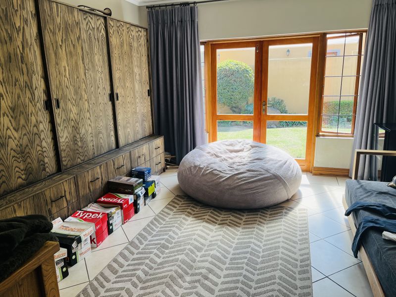 A living room featuring built-in wooden cabinetry, tiled flooring, and large wooden framed double doors providing access to the garden.