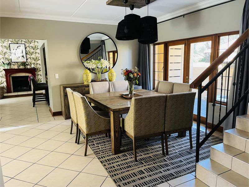 Spacious dining area featuring tiled floors, a wooden staircase with wrought iron balustrade, and direct access to the patio through wooden framed glass doors.