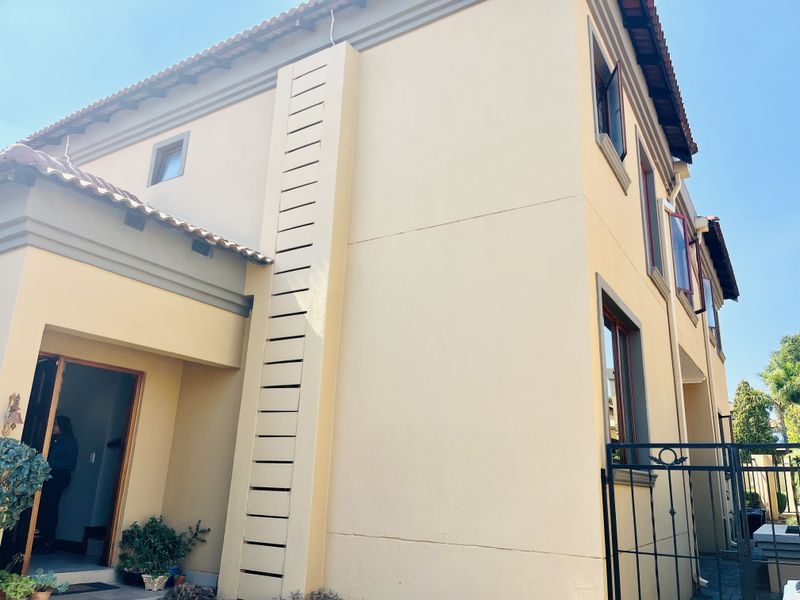 A view of the front facade of the cluster home, featuring a plastered exterior, tiled roof, and secure metal gate entrance.