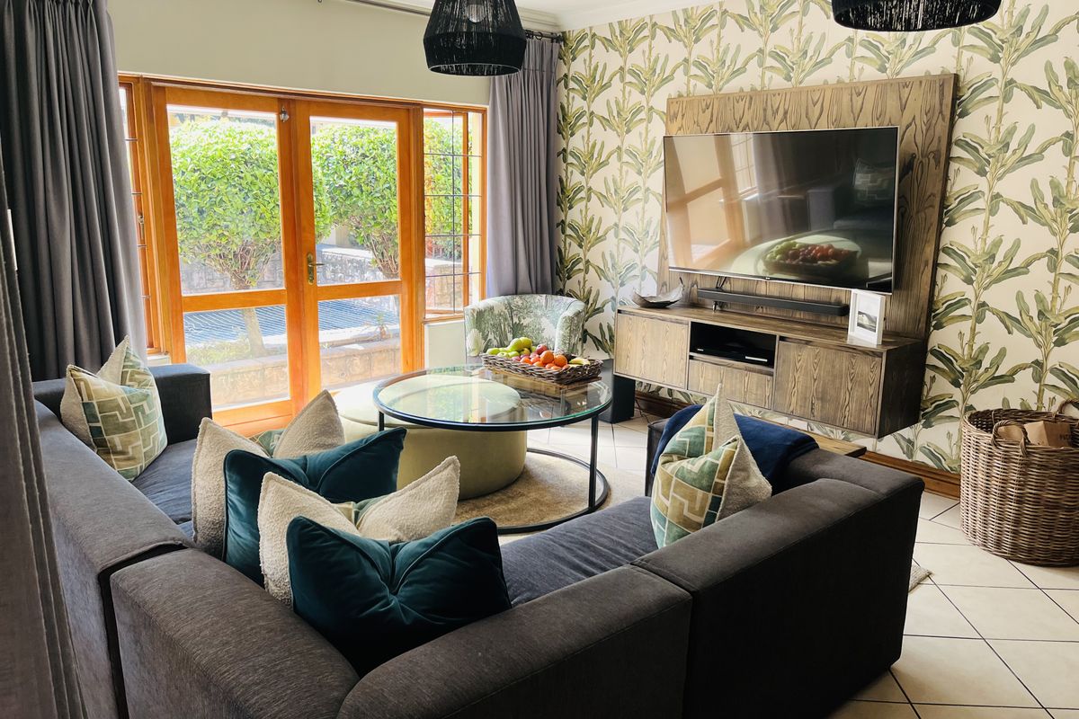 A well-maintained living room featuring a built-in media unit, tiled flooring, and wooden framed glass doors providing access to the outdoor area.