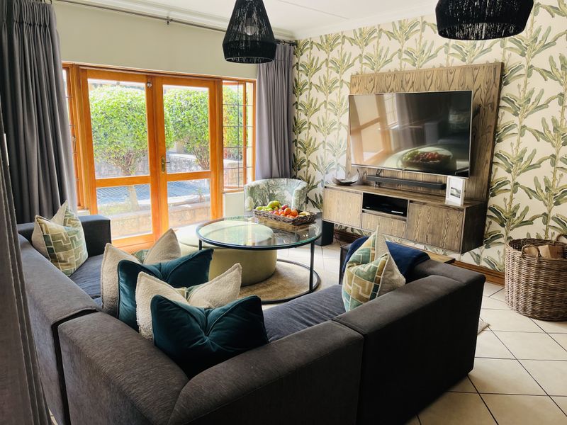 A well-maintained living room featuring a built-in media unit, tiled flooring, and wooden framed glass doors providing access to the outdoor area.