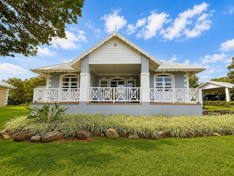 A well-maintained rear elevation featuring a covered patio with timber balustrades, set within a neatly landscaped garden.