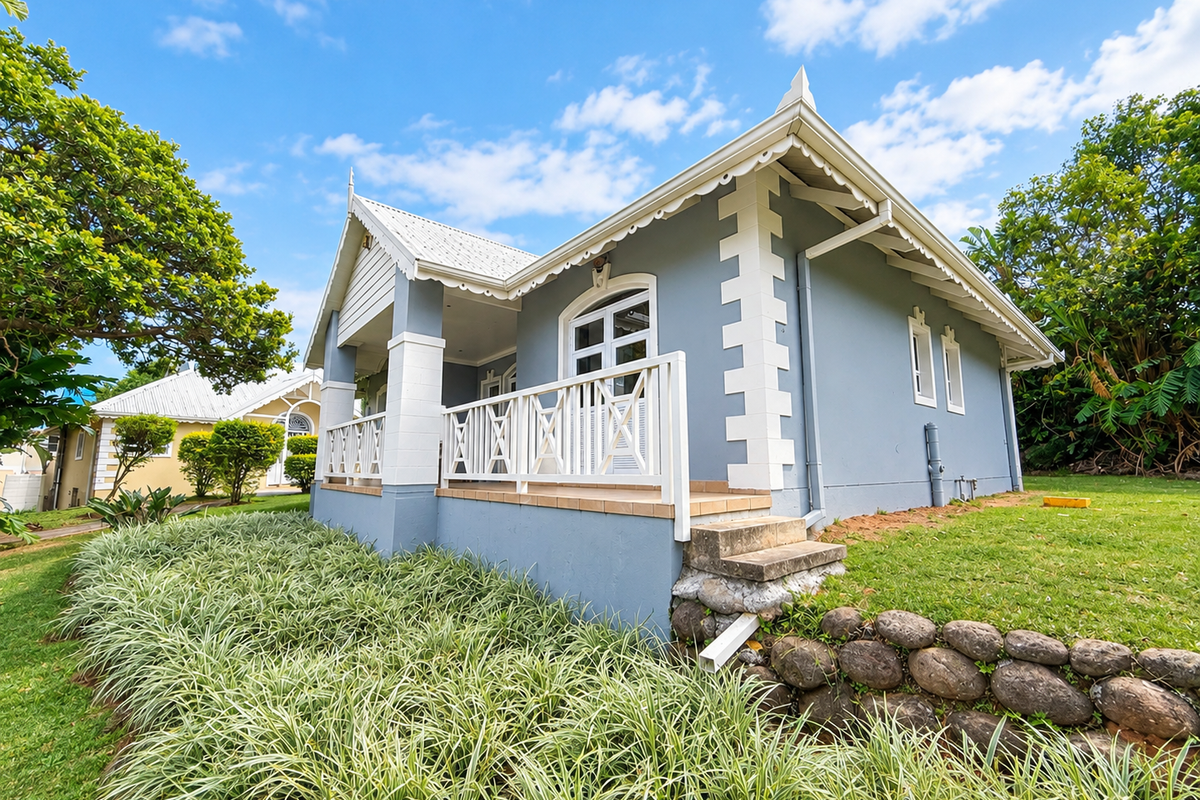 A well-maintained cottage-style home featuring a covered patio with timber balustrades, set against a landscaped garden with a stone retaining wall.