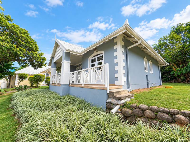 A well-maintained cottage-style home featuring a covered patio with timber balustrades, set against a landscaped garden with a stone retaining wall.