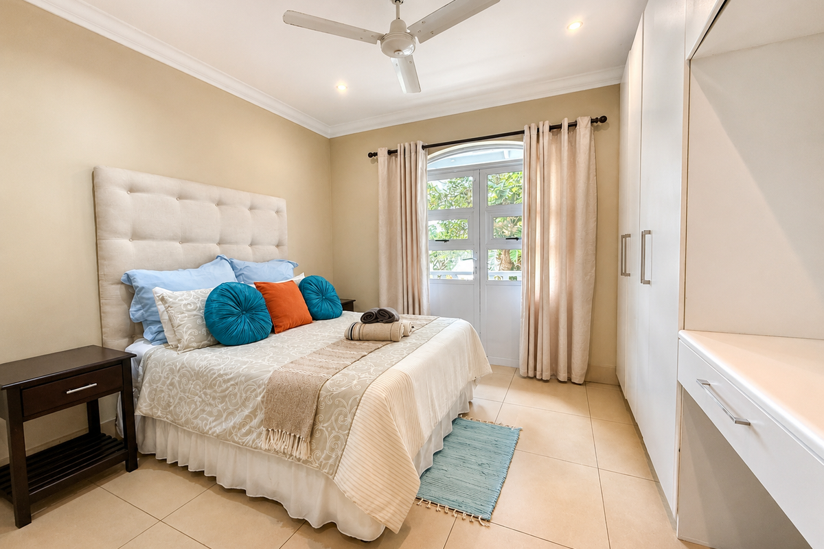 A well-maintained bedroom featuring tiled flooring, built-in cupboards, a built-in vanity, and an arch-top glass door providing natural light.