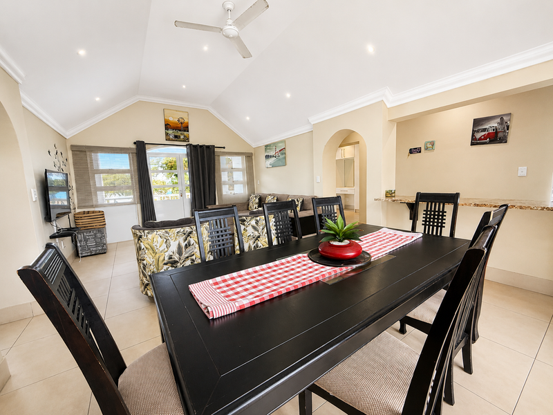 Spacious open-plan living and dining area featuring a vaulted ceiling, tiled flooring, and a breakfast bar with an arched transition to the kitchen.