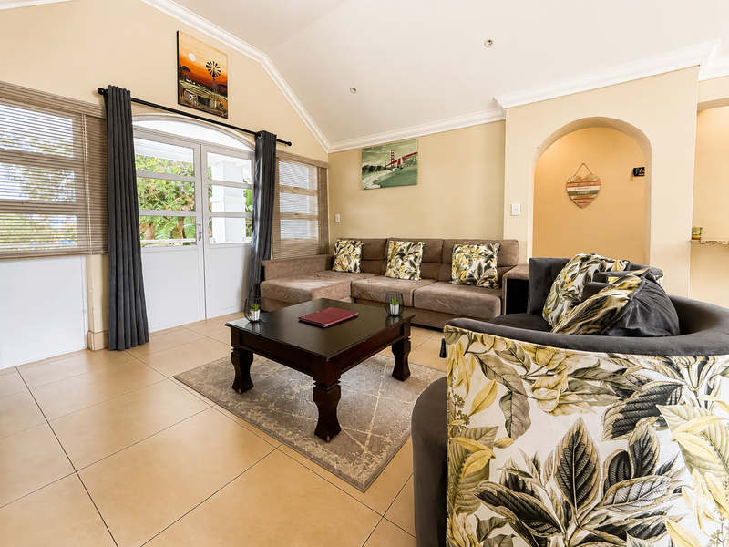 A bright living room featuring a vaulted ceiling, tiled flooring, and an elegant archway leading to an adjacent space, with access to the outdoors.