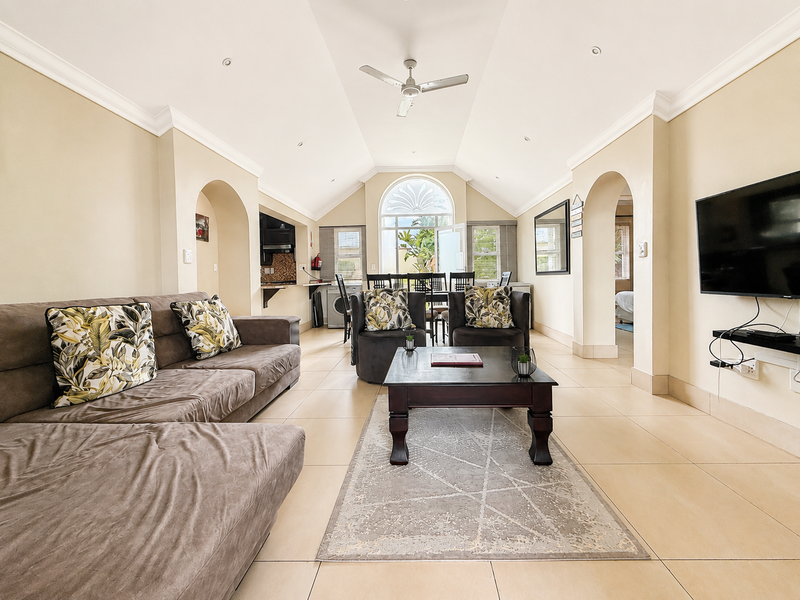 Spacious open-plan living area featuring vaulted ceilings, tiled flooring, and an arched window, seamlessly connecting to the kitchen and dining space.
