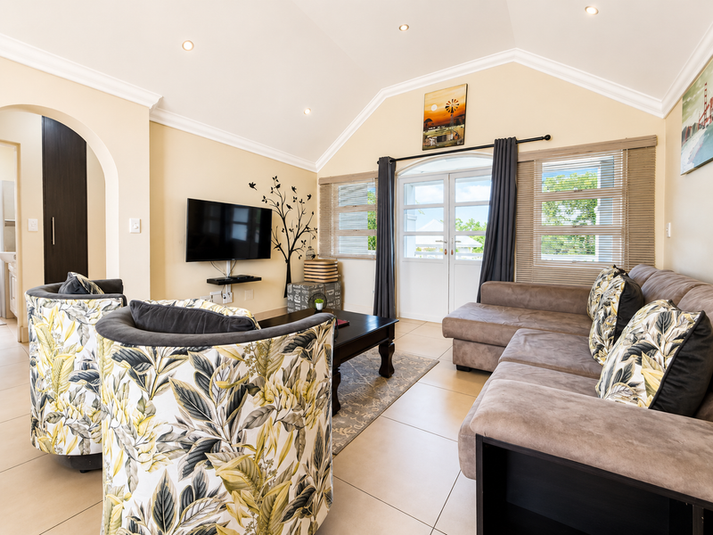 A bright living room featuring a vaulted ceiling, tiled flooring, and double glass doors leading to an outdoor area.