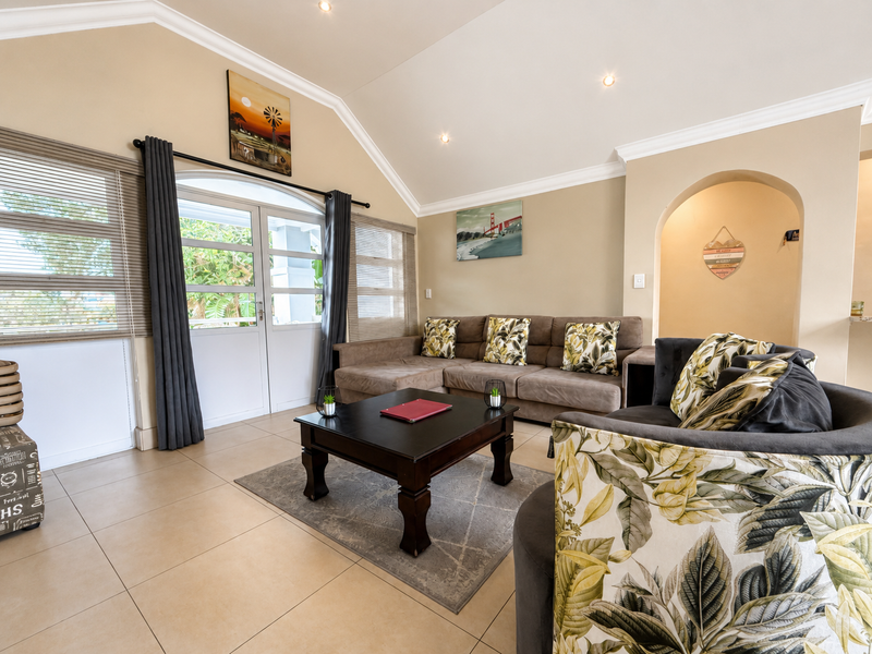 Spacious living room featuring a vaulted ceiling, tiled flooring, and an elegant archway leading to adjacent areas, with natural light from double glass doors.