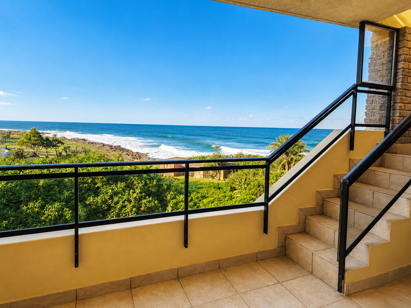 A spacious balcony featuring tiled flooring and a metal balustrade, offering expansive, unobstructed views of the ocean and coastline.
