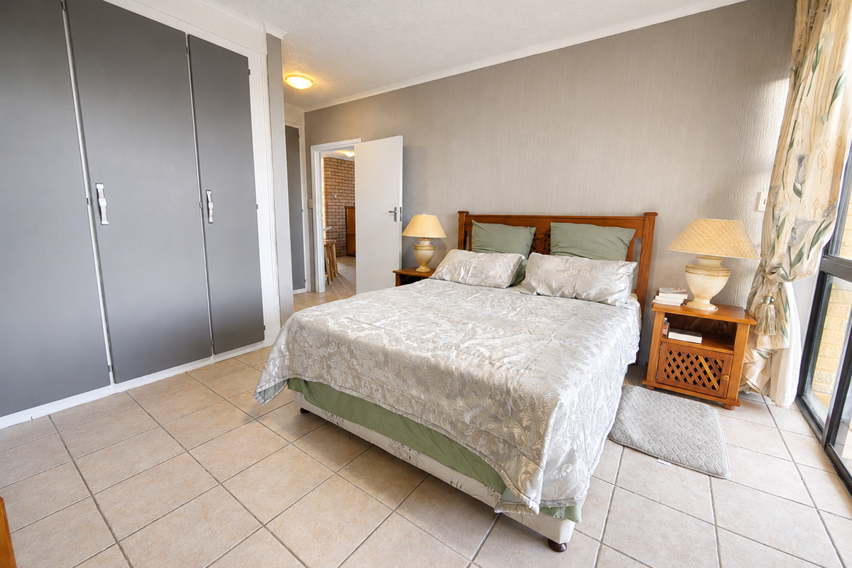 A bedroom featuring built-in cupboards, tiled flooring, and a sliding glass door providing natural light.