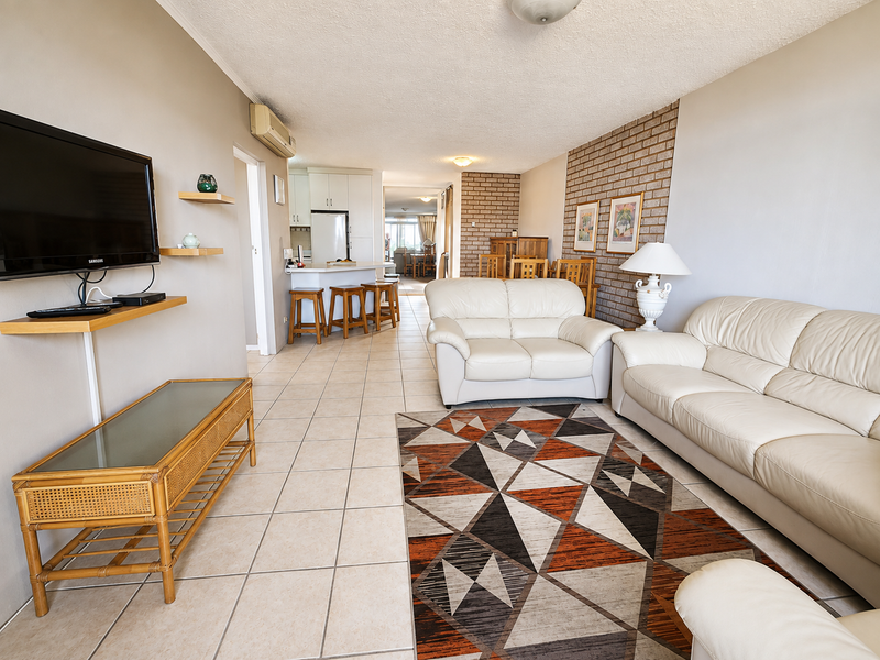 Spacious open-plan living area featuring tiled floors, a brick feature wall, and a functional kitchen with a breakfast bar.