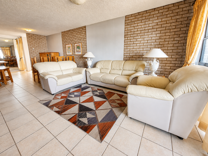 Spacious living area featuring a textured ceiling, ceramic floor tiles, and a prominent exposed brick feature wall.
