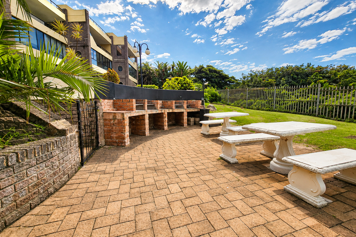 Communal outdoor entertainment area featuring a built-in brick braai, paved patio space, and established garden surroundings.