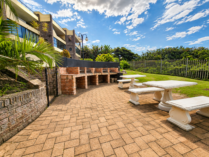 Communal outdoor entertainment area featuring a built-in brick braai, paved patio space, and established garden surroundings.