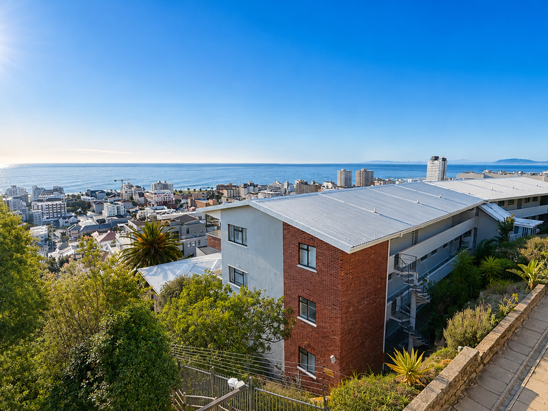 Elevated aerial view of the apartment complex featuring a metal roof, brick exterior, and surrounding landscaped grounds with a scenic coastal outlook.