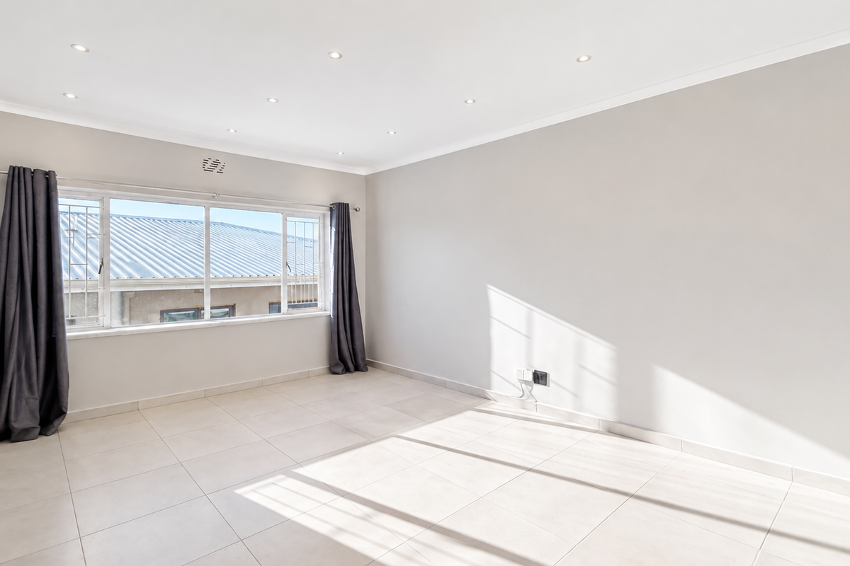 A bright, empty bedroom featuring neutral tiled flooring, recessed downlighting, and large windows with security bars.