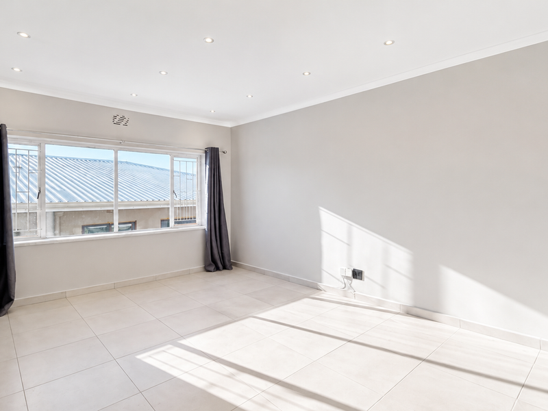 A bright, empty bedroom featuring neutral tiled flooring, recessed downlighting, and large windows with security bars.