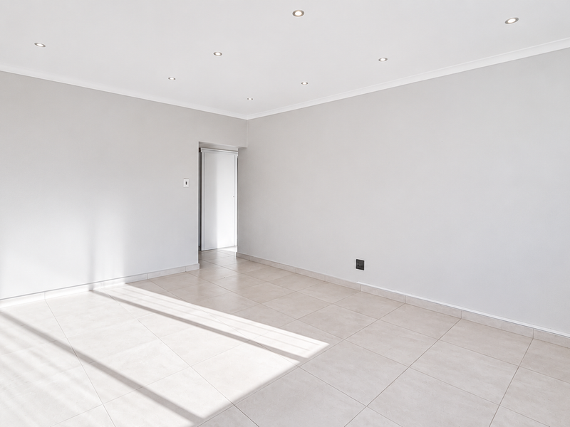 A bright, empty living area featuring neutral ceramic floor tiles, recessed downlighting, and clean, freshly painted walls.