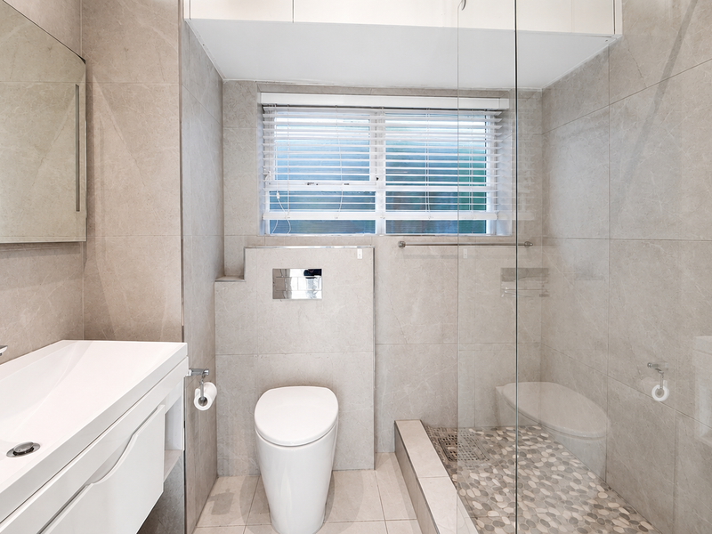 Modern bathroom featuring a wall-mounted vanity, concealed cistern toilet, and a spacious walk-in shower with a glass screen and pebble tile flooring.