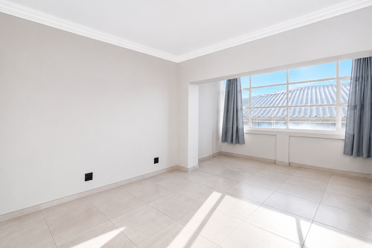 A bright and spacious empty living area featuring neutral tiled flooring, large windows, and clean white walls, ready for personalization.