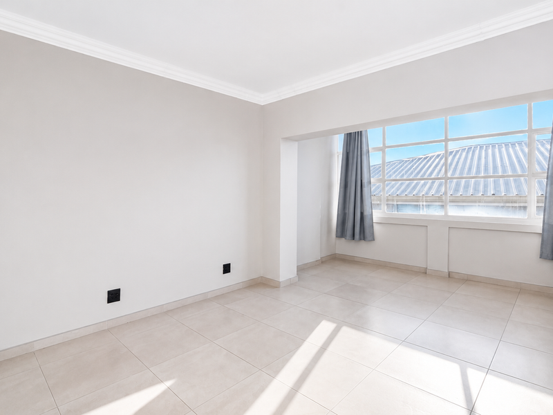 A bright and spacious empty living area featuring neutral tiled flooring, large windows, and clean white walls, ready for personalization.