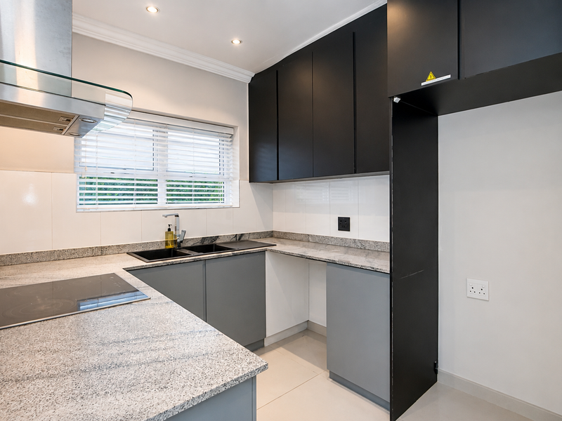 Modern kitchen featuring sleek black and grey cabinetry, granite countertops, a built-in electric hob, stainless steel extractor fan, and tiled flooring.