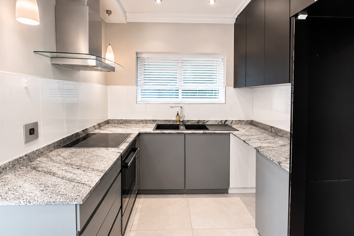 Modern kitchen featuring granite countertops, sleek grey cabinetry, stainless steel extractor fan, built-in oven, and a double sink with a mixer tap.