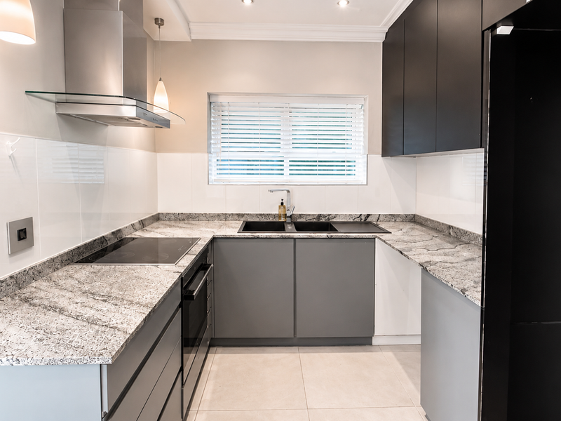 Modern kitchen featuring granite countertops, sleek grey cabinetry, stainless steel extractor fan, built-in oven, and a double sink with a mixer tap.