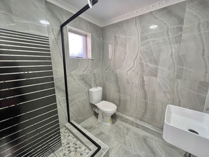 Modern bathroom featuring large-format grey marble-look tiles, a walk-in shower with a black-framed glass screen, a wall-mounted basin, and a contemporary toilet.