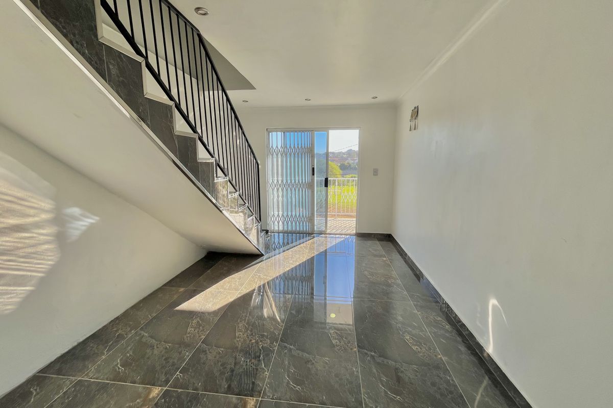 An open-plan living area featuring polished dark tiles, a modern staircase with a metal balustrade, and a sliding door leading to an outdoor space.