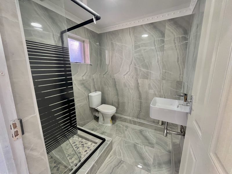Modern bathroom featuring floor-to-ceiling marble-look tiling, a walk-in shower with a glass screen, a wall-mounted basin, and a toilet.