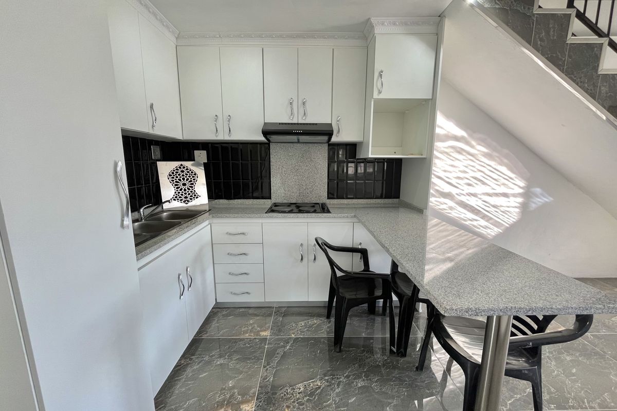 Modern kitchen featuring white cabinetry, granite countertops, a breakfast bar, and dark tiled flooring, situated conveniently under the staircase.