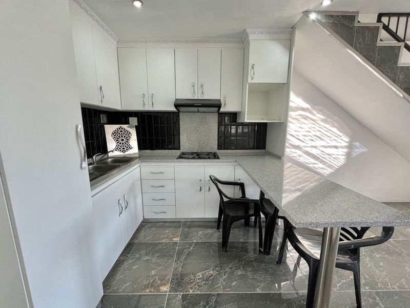 Modern kitchen featuring white cabinetry, granite countertops, a breakfast bar, and dark tiled flooring, situated conveniently under the staircase.