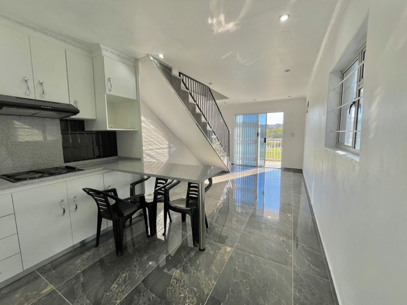 Modern open-plan kitchen and living area featuring sleek cabinetry, granite countertops, polished tiled floors, and a staircase leading to the upper level.