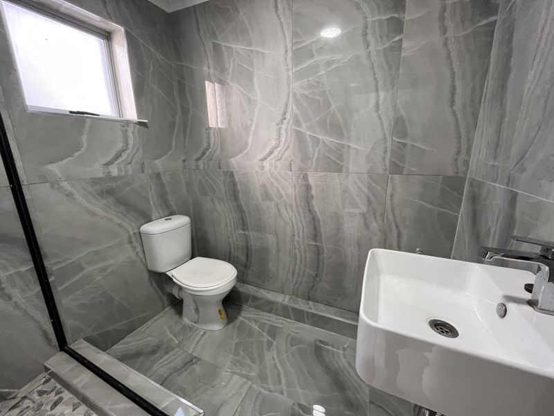Modern bathroom featuring large-format grey marble-effect porcelain tiles, a contemporary wall-mounted basin with mixer tap, and a standard toilet.