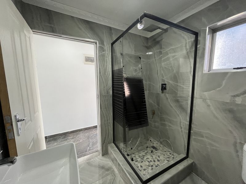Modern bathroom featuring a walk-in shower with a black-framed glass enclosure, rain shower head, and contemporary grey marble-look porcelain tiling throughout.