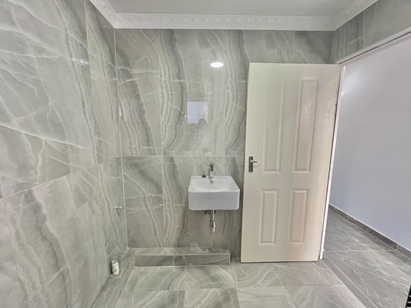 A modern bathroom featuring large-format grey marble-effect porcelain tiles, a wall-mounted basin with chrome fixtures, and recessed lighting.