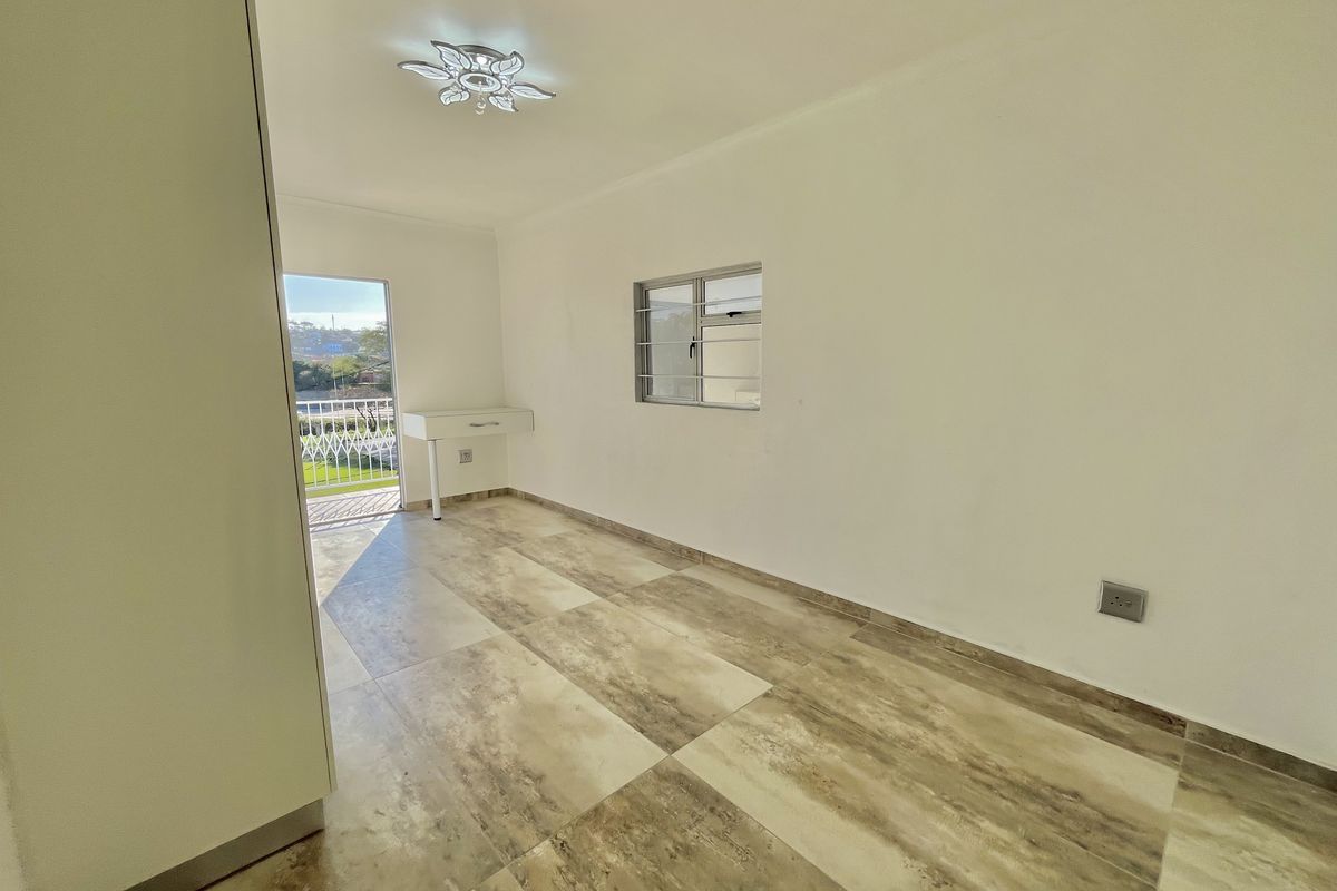A bright, empty bedroom featuring modern tiled flooring, a built-in vanity, and direct access to a private balcony through a sliding door.