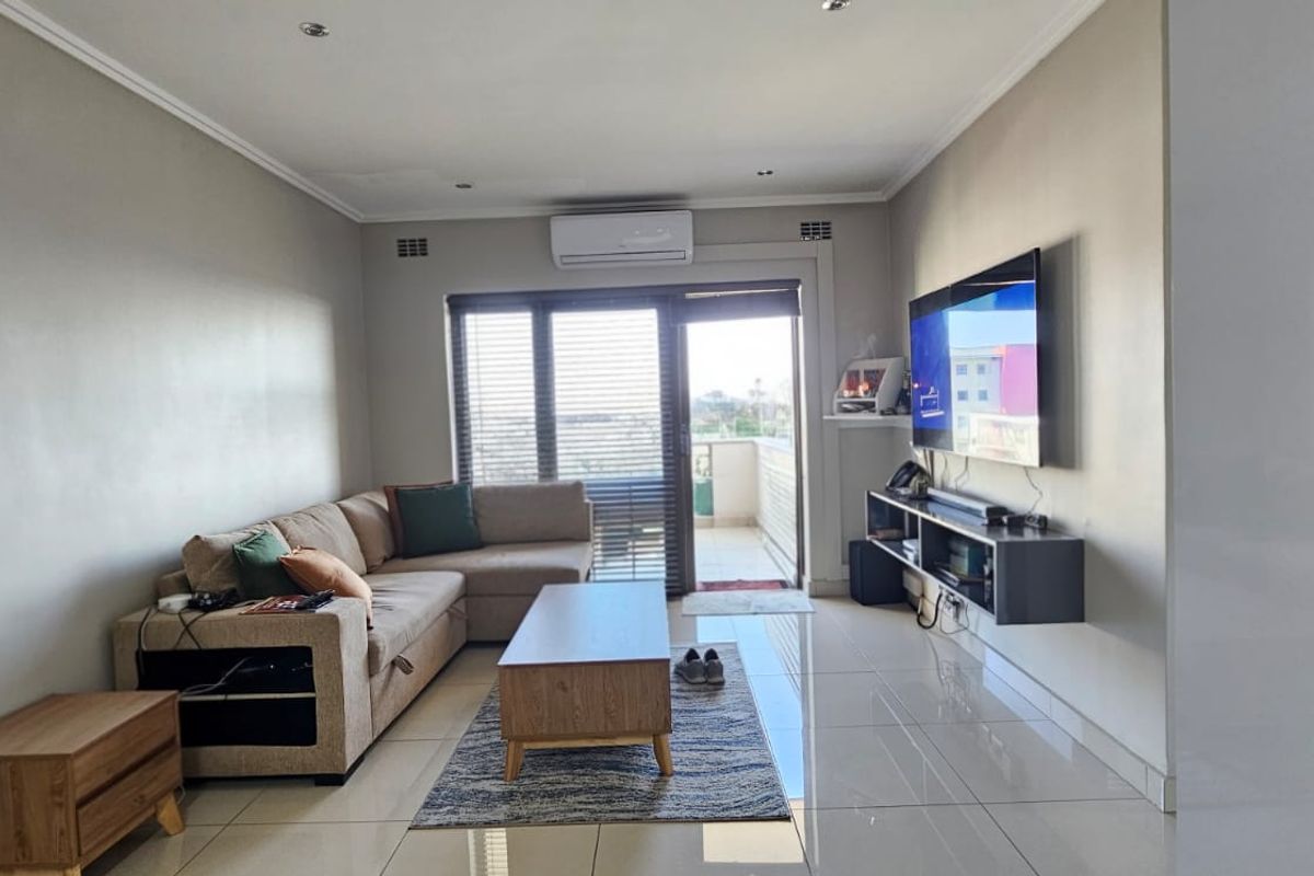 Modern living room featuring polished tiled flooring, recessed downlighting, a wall-mounted air conditioning unit, and direct access to a balcony through sliding glass doors.
