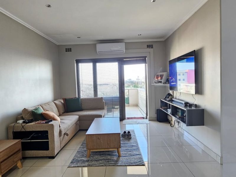 Modern living room featuring polished tiled flooring, recessed downlighting, a wall-mounted air conditioning unit, and direct access to a balcony through sliding glass doors.
