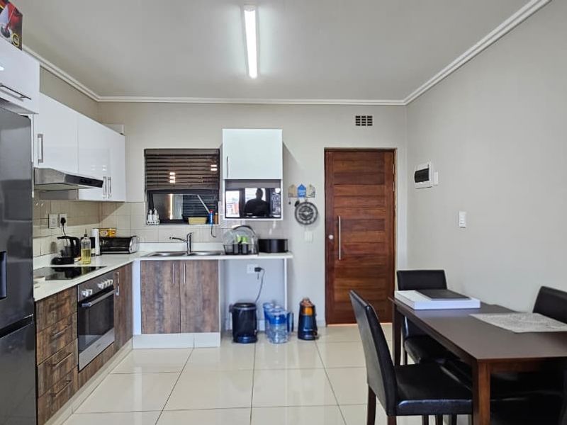 Modern open-plan kitchen and dining area featuring sleek cabinetry, built-in appliances, tiled flooring, and a solid wooden door.