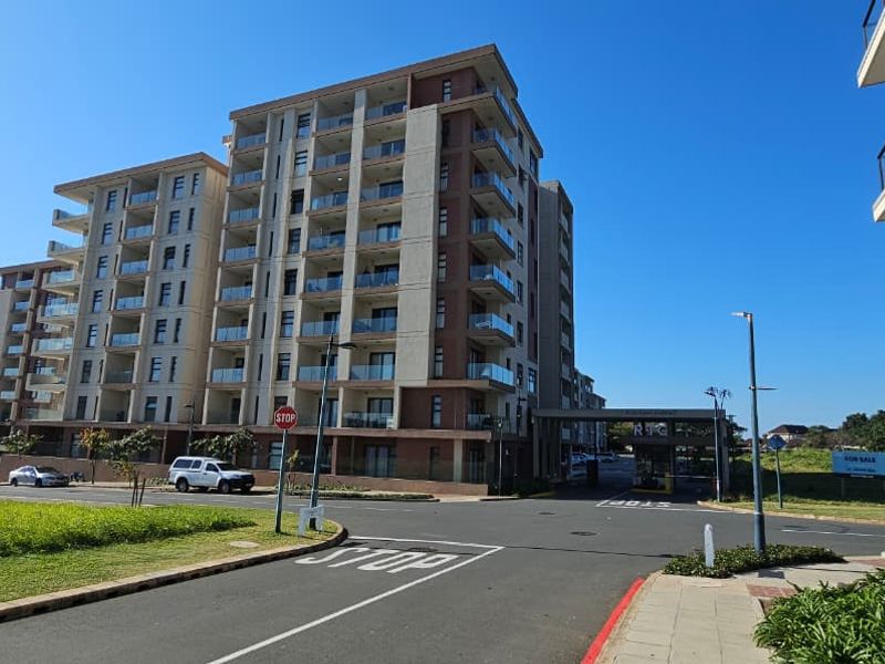 A modern multi-story apartment complex featuring glass balconies and a secure gated entrance, situated in a well-maintained residential estate.
