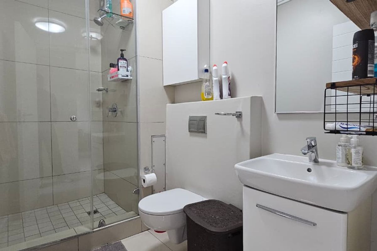 A modern bathroom featuring a glass-enclosed shower, wall-mounted toilet, and a vanity basin with storage.