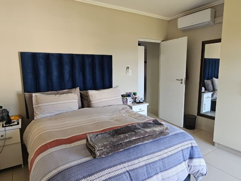 A well-maintained bedroom featuring built-in cupboards, tiled flooring, and a wall-mounted air conditioning unit.